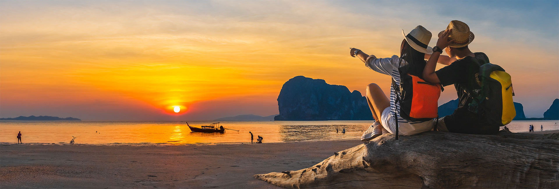 Two travel nurses sitting on the shore watching the sun set over the water as boats pass by.