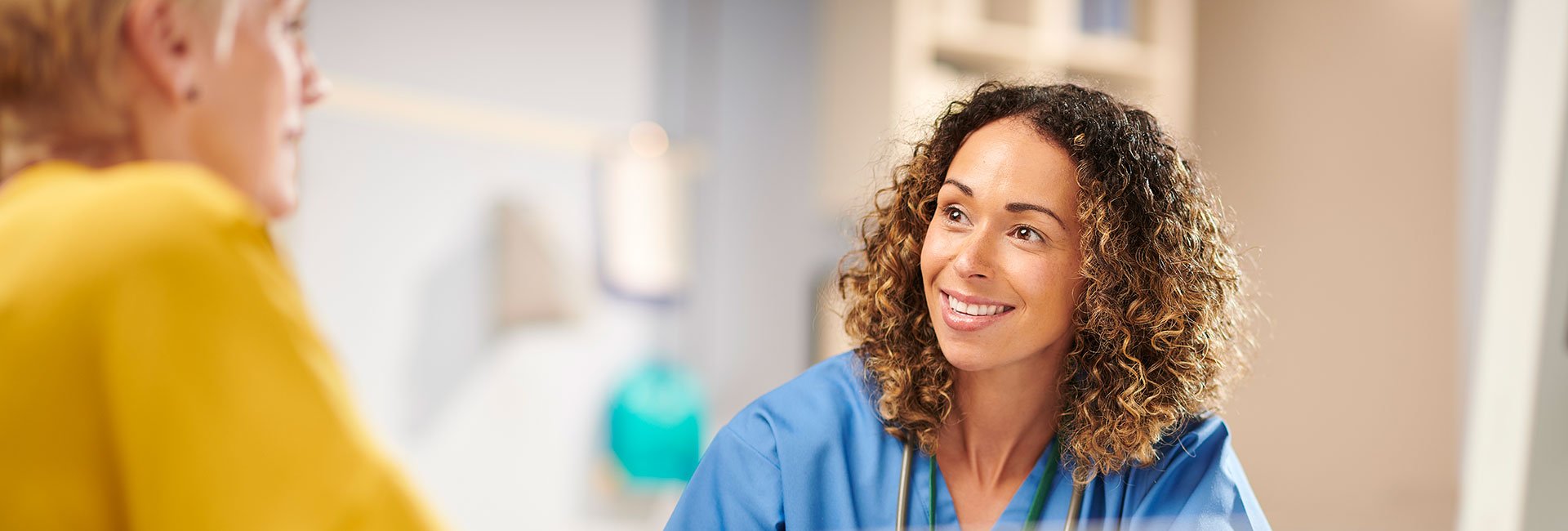 Female travel nurse with curly hair speaking with patient.